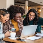 American women celebrating financial success together while reviewing money-saving challenges on laptop