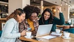 American women celebrating financial success together while reviewing money-saving challenges on laptop